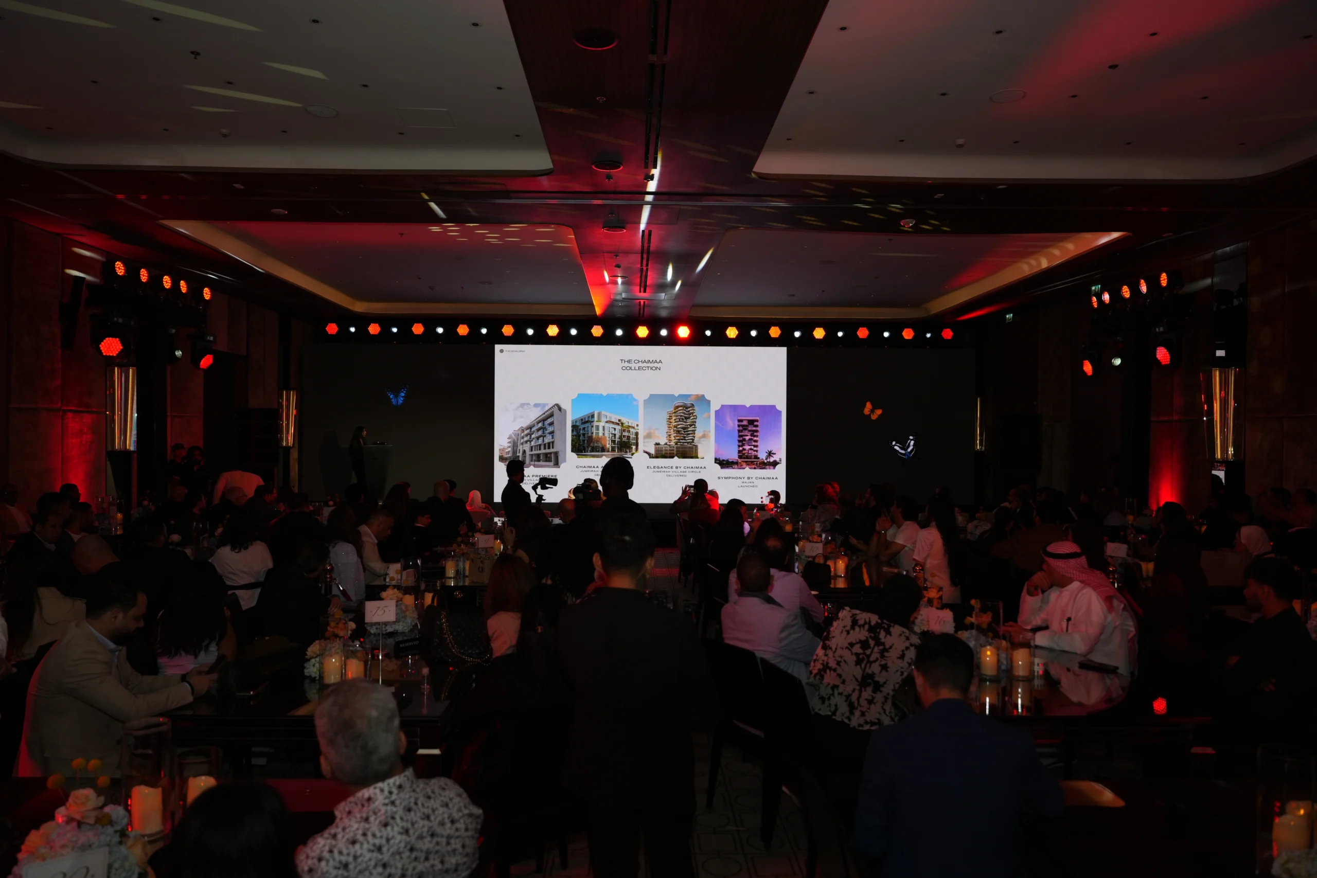 Chaimaa Collection real estate launch event at Bvlgari Hotel Dubai with an engaged audience, property presentation on a large LED screen and warm red ambient lighting