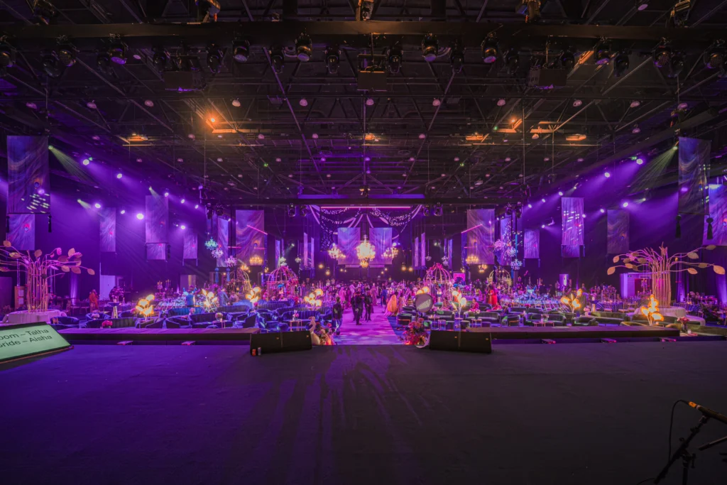 A breathtaking grand wedding hall at Madinat Jumeirah with sweeping purple lighting, decorative floral installations, crystal chandeliers and elegant lounge seating for hundreds of guests