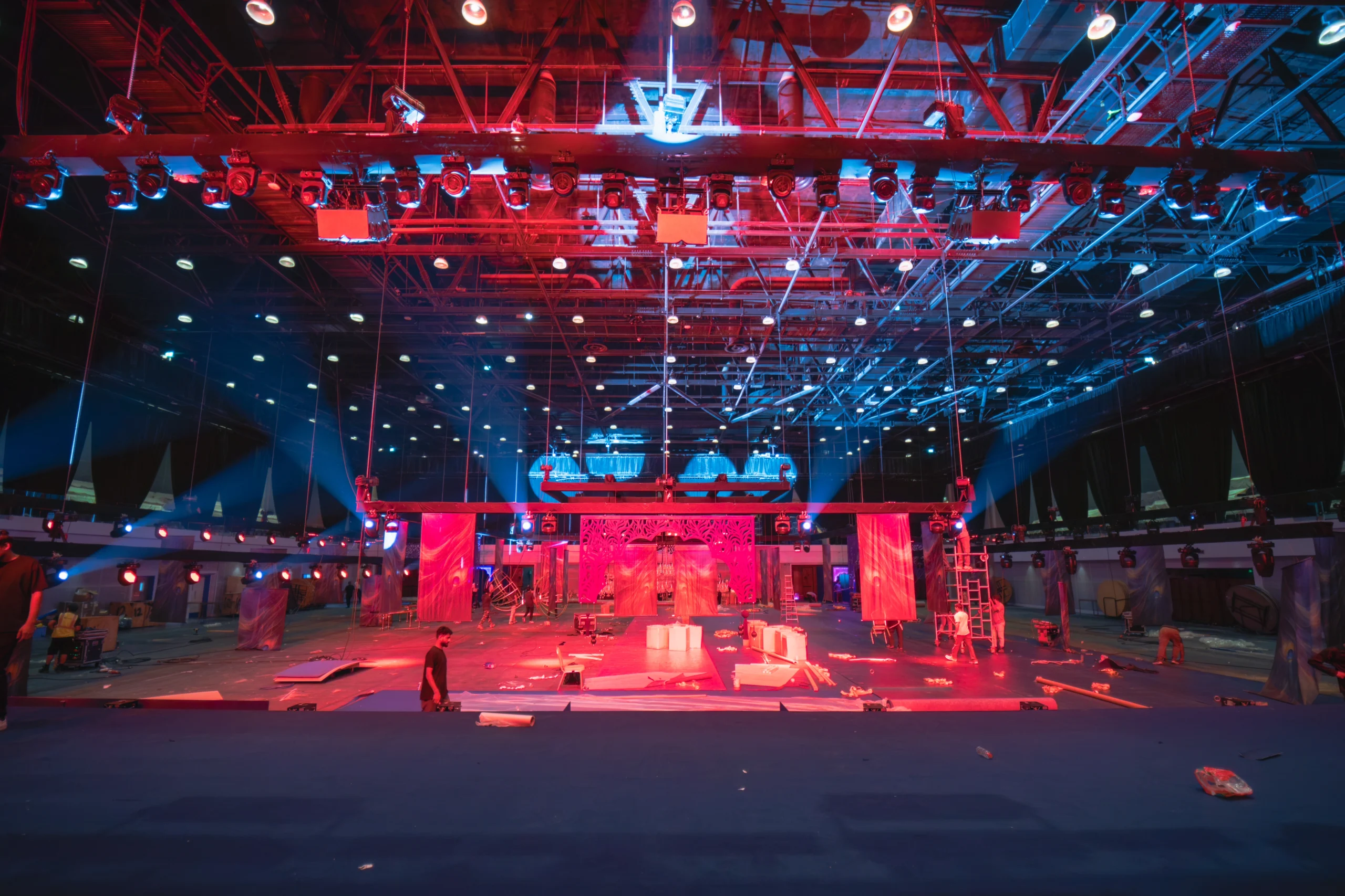 Behind the scenes setup of a grand wedding event at Madinat Jumeirah with professional rigging, red and blue stage lighting and an ornate laser-cut backdrop under construction