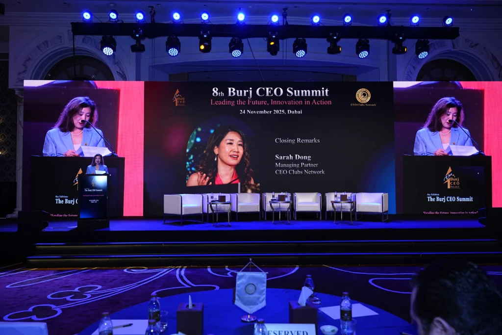 A speaker delivering closing remarks at the 8th Burj CEO Summit in Dubai with a large branded LED screen and panel seating on a professional conference stage