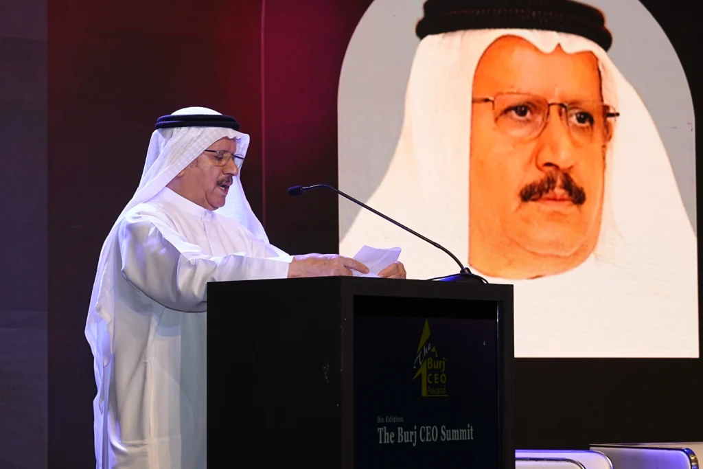 An Emirati speaker delivering a keynote address at the 8th Burj CEO Summit podium with a large portrait screen in the background