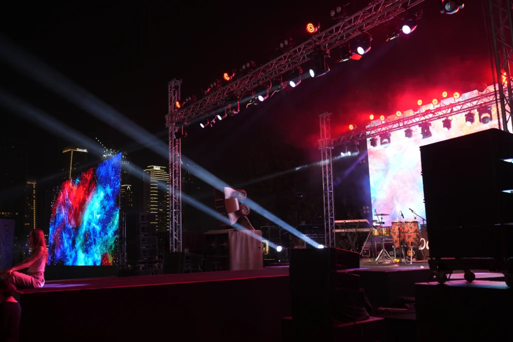 An outdoor beachfront concert stage at Barasti Beach Dubai with vibrant LED video walls, professional truss lighting and the iconic Emaar skyline in the background