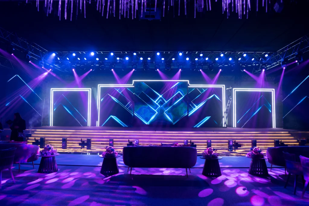A stunning Megawatt Live event stage featuring vibrant LED lights, glowing neon geometric backdrop and elegant lounge seating