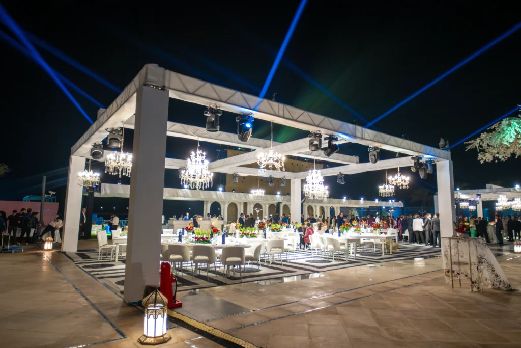 A breathtaking outdoor Qatar wedding reception with crystal chandeliers, elegant white dining tables, floral centerpieces and dramatic blue laser lights in the night sky