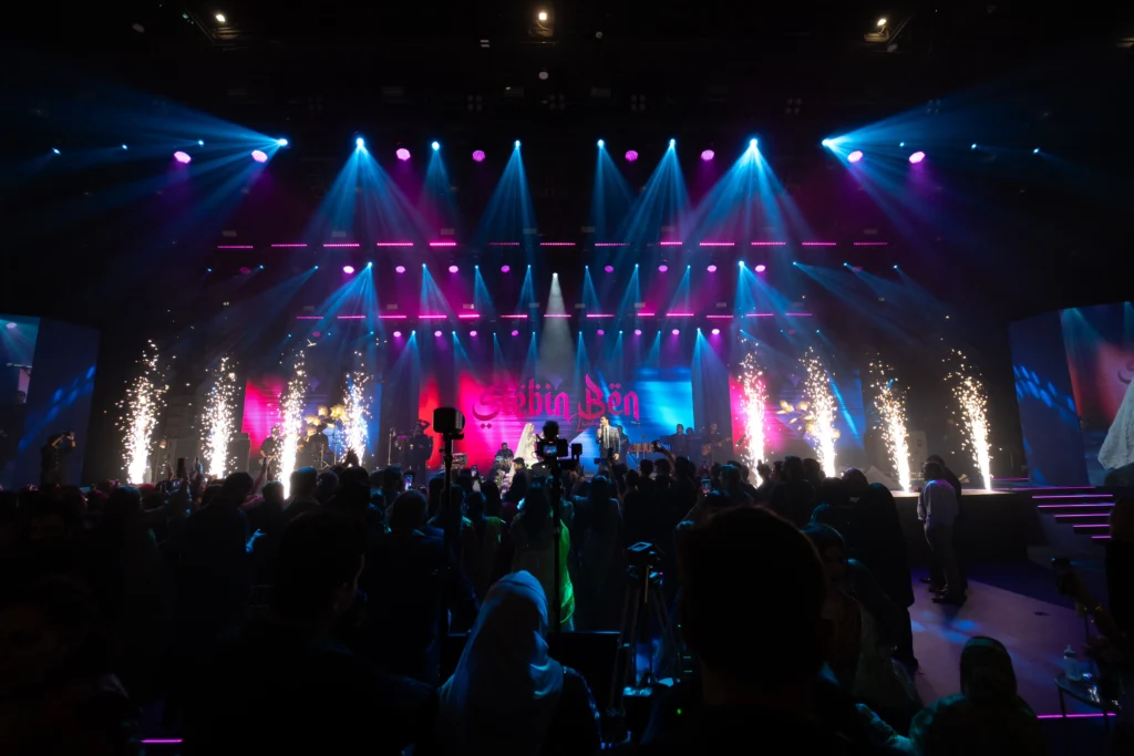 A bride and groom entering a grand wedding stage with spectacular pyrotechnic sparks, vibrant LED lights and a live band performing for the audience