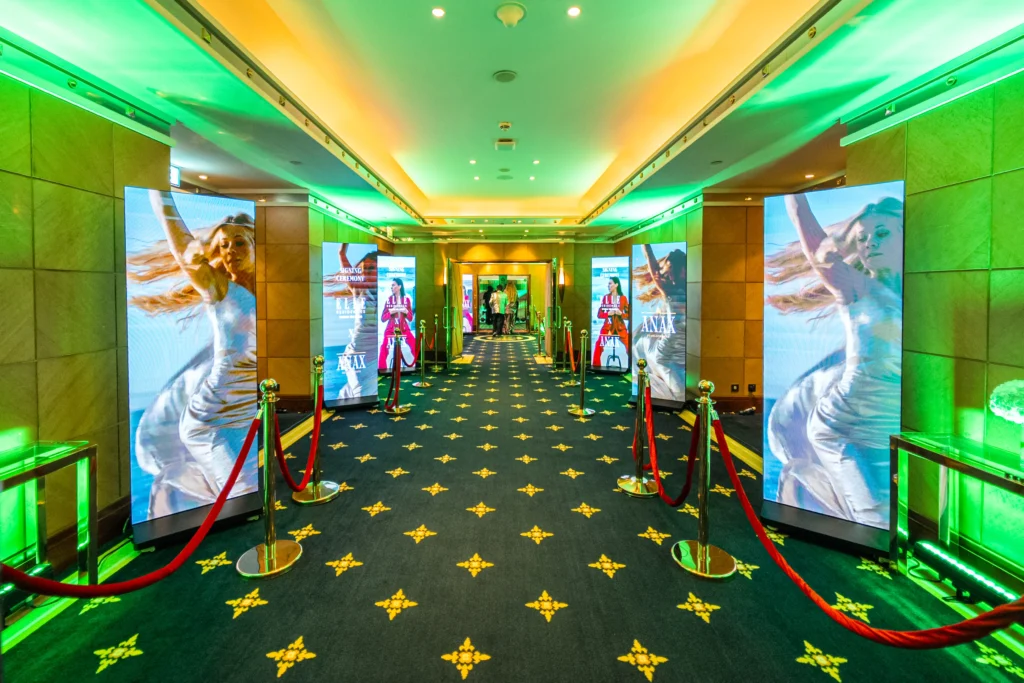 Elle Residences x Anax Developments signing ceremony entrance corridor with tall LED fashion screens, red velvet ropes and green ambient lighting in a luxury Dubai hotel