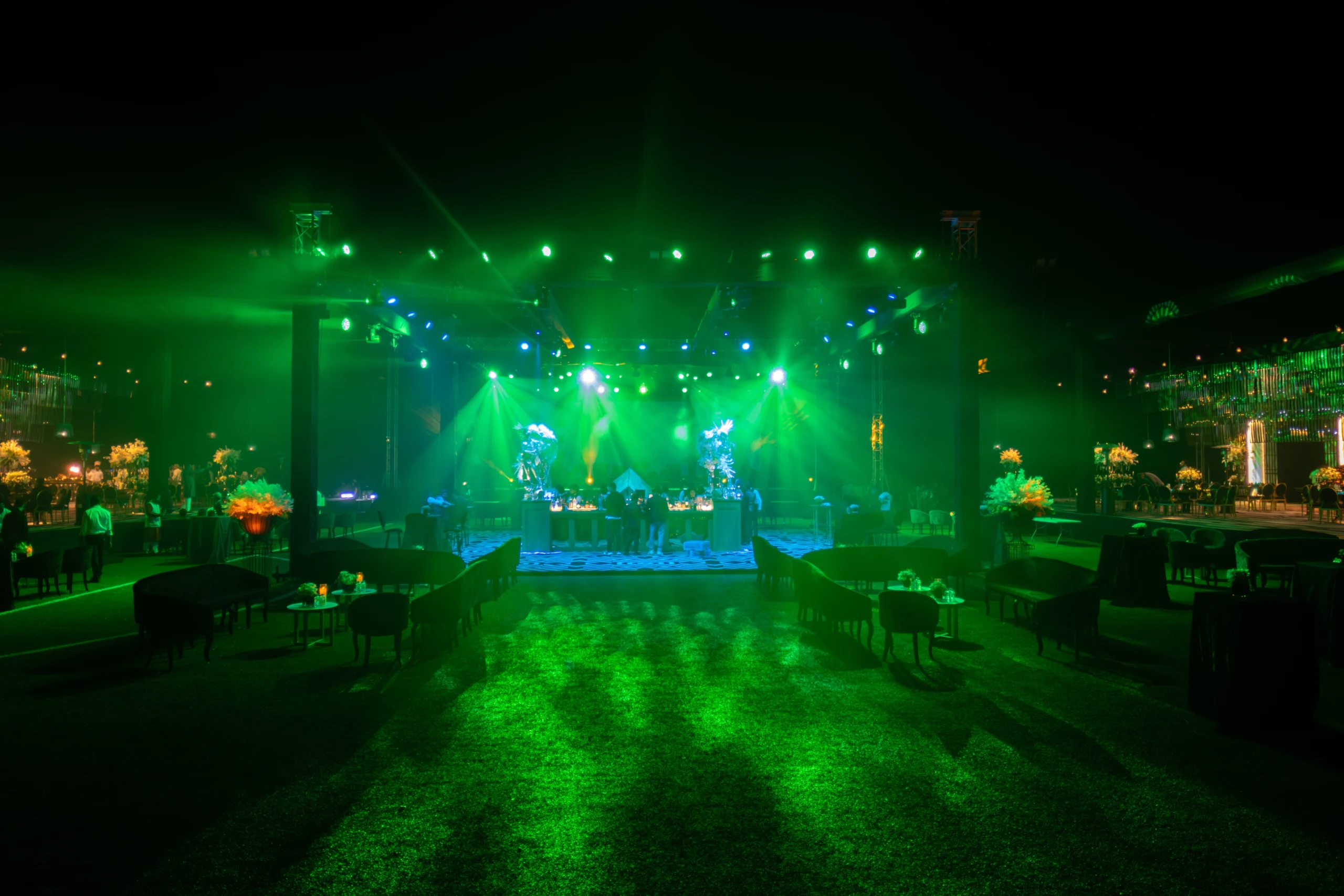 An enchanting Qatar wedding event hall with lush green stage lighting, artificial grass flooring, colorful floral arrangements and an elegant center stage